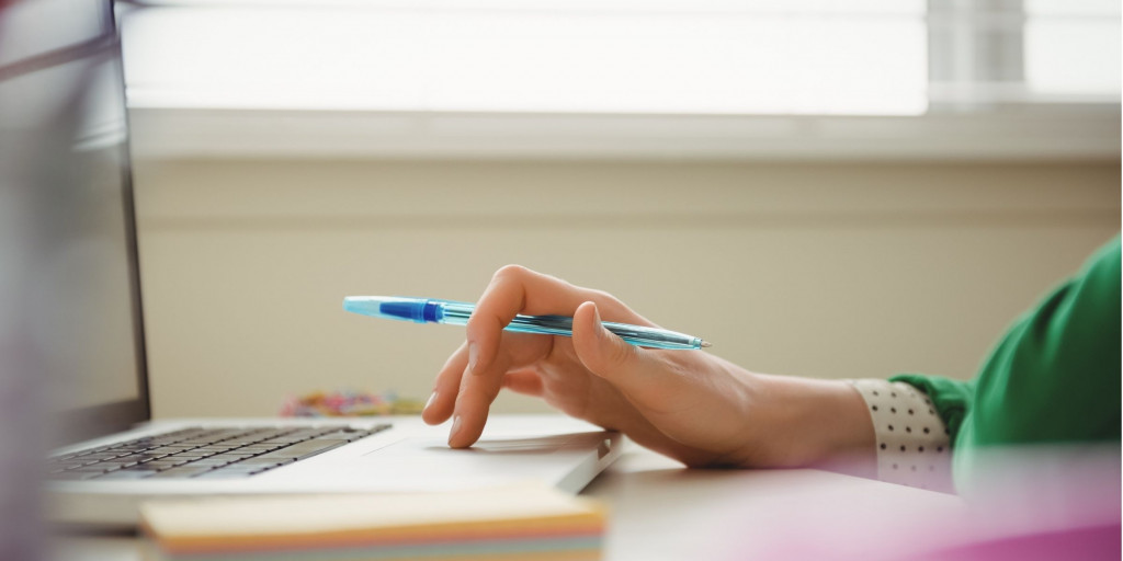 Vrouw aan het werken op een laptop met stylo in de hand. Haar gezicht is niet zichtbaar.