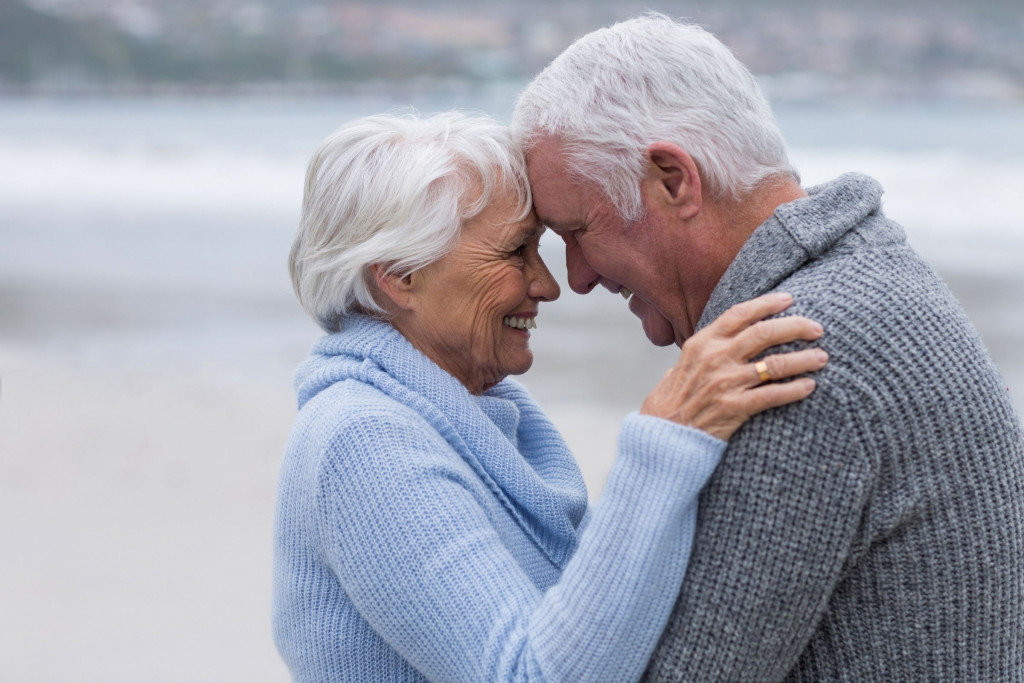 Ouder koppel knuffelt op het strand