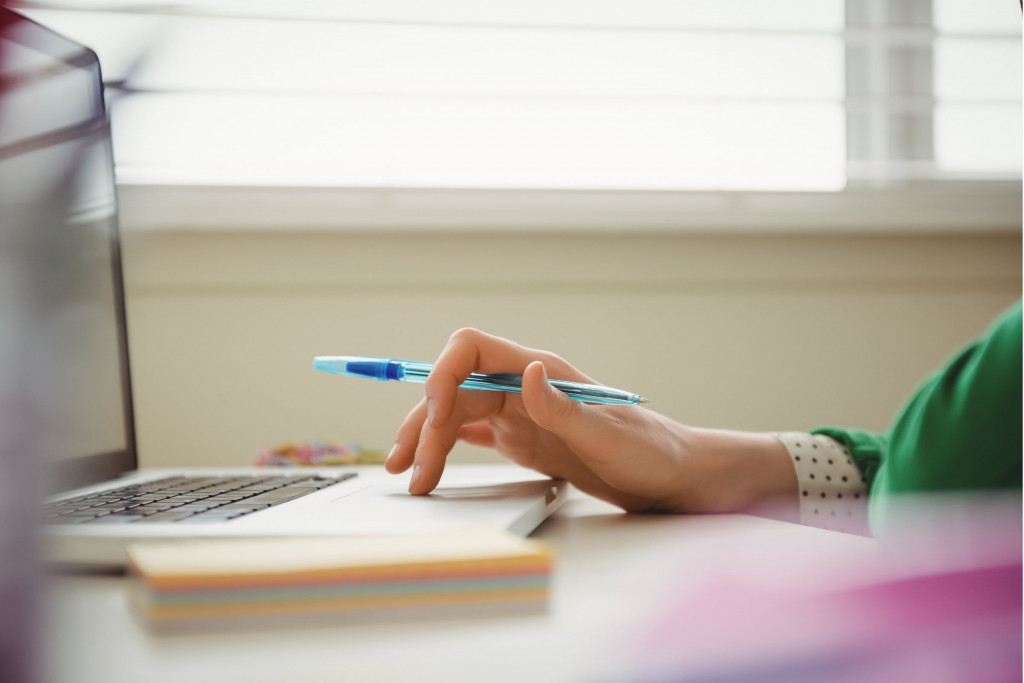 Vrouw aan het werken op een laptop met stylo in de hand. Haar gezicht is niet zichtbaar.