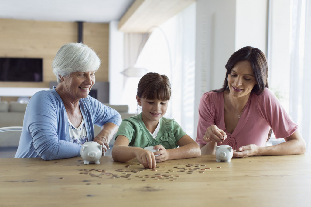 Grootmoeder met kleinkind en dochter aan een tafel waarop een spaarpot staat